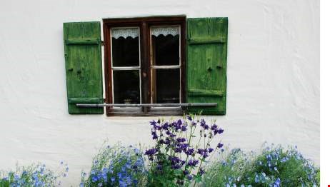Stenhus med ett fönster. Under fönstret finns en blomrabatt med blå-lila blommor i. 